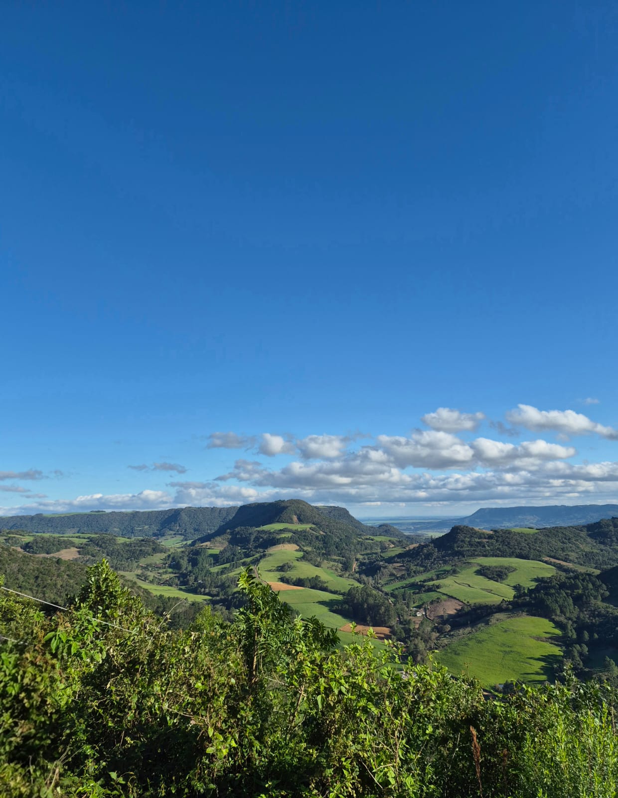 Vista vertical dos morros verdes da Quarta Colônia sob um amplo céu azul