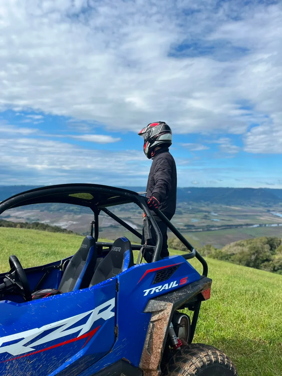 Pessoa ao lado do Polaris RZR azul olhando o vale da Quarta Colônia