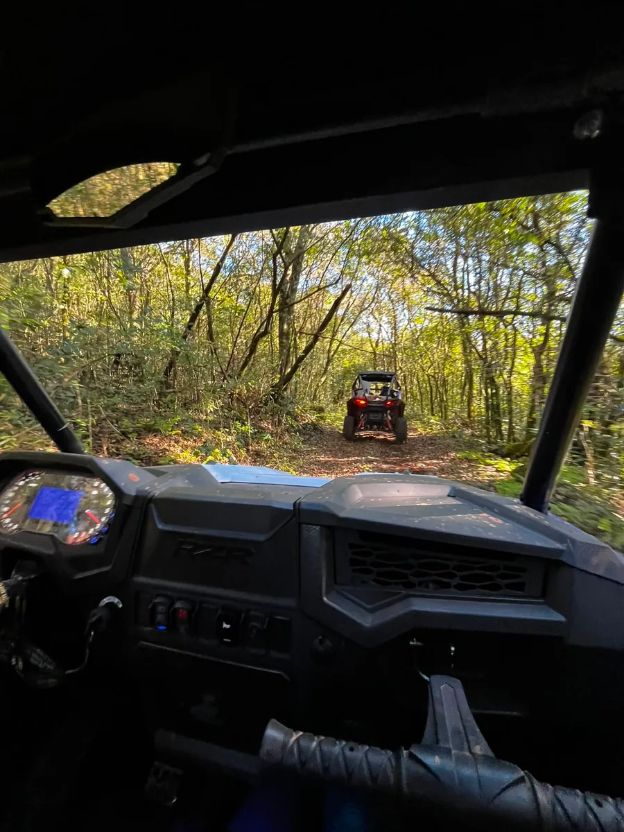 Vista do interior do UTV, painel e trilha de mata à frente com outro veículo