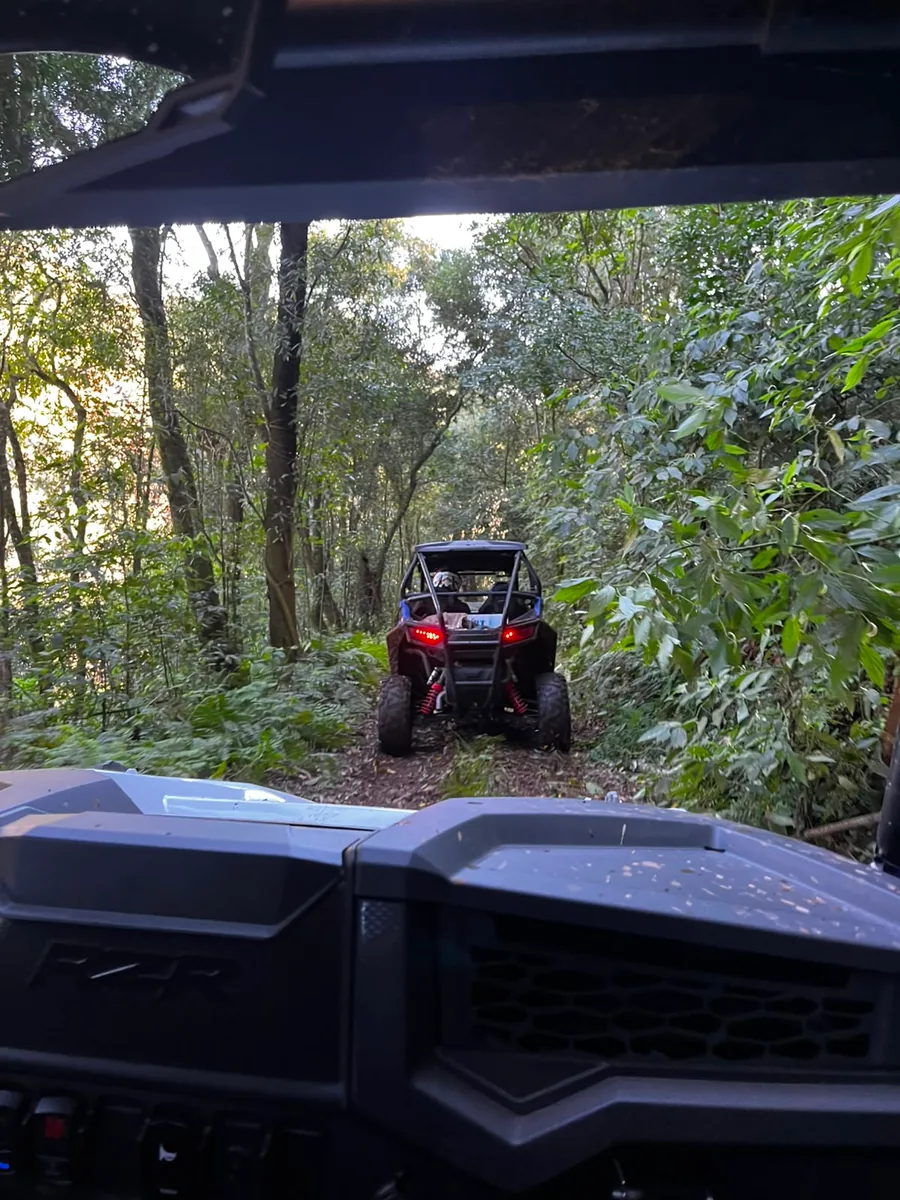 UTV vermelho à frente do comboio numa trilha estreita de mata fechada