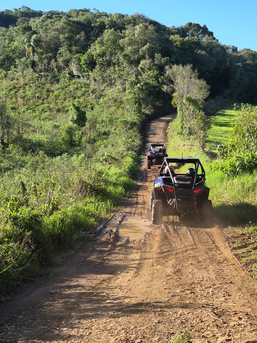 UTV subindo uma trilha de terra entre morros verdes, levantando poeira