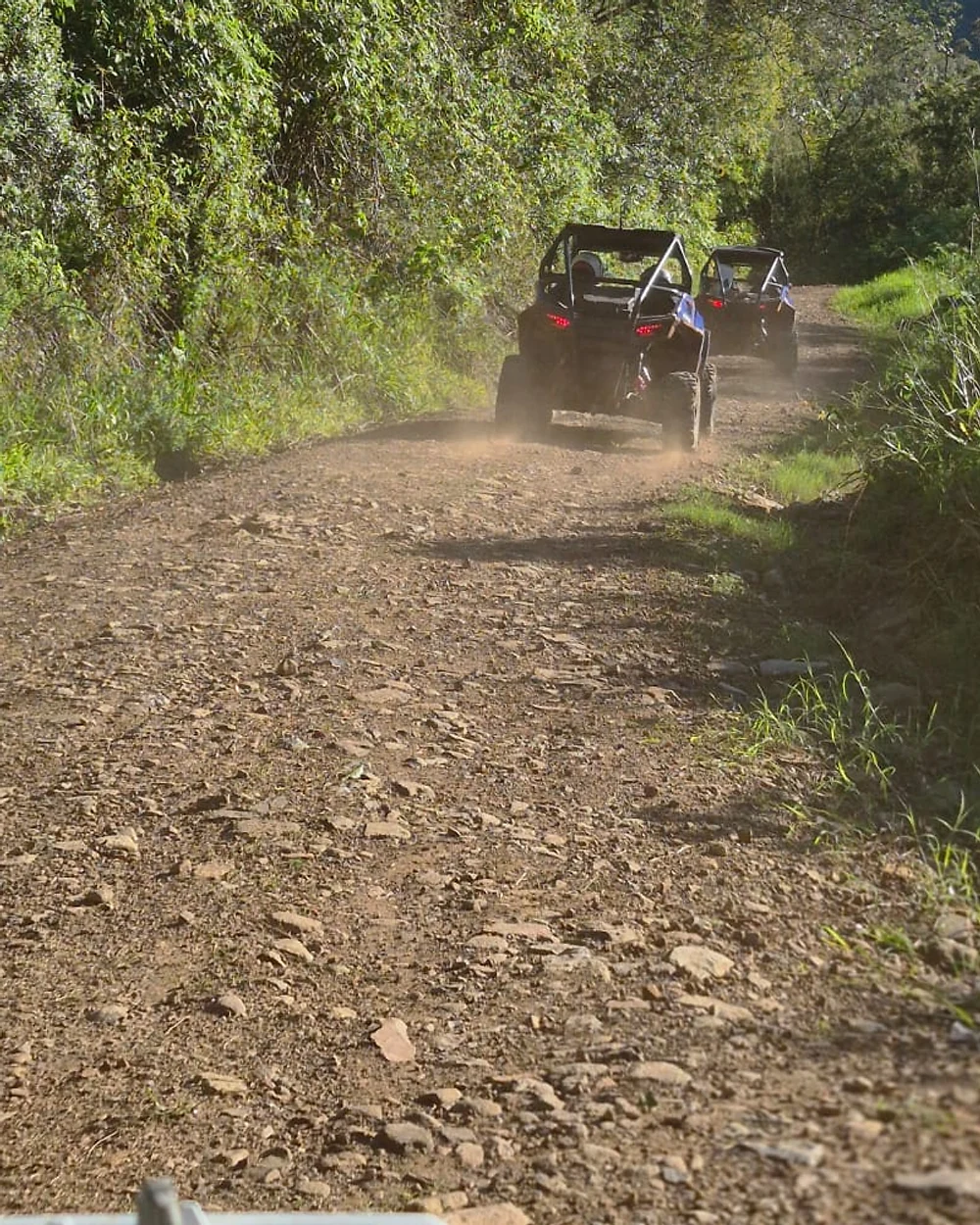 Estrada tomada por cascalho e pedra solta, com os UTVs subindo ao fundo